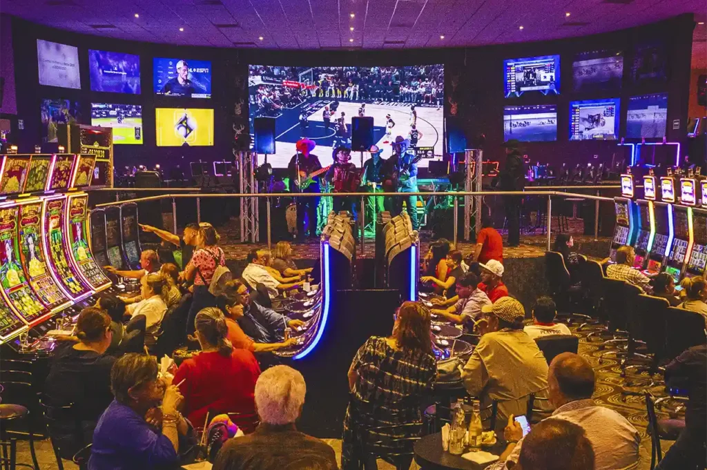 Área del casino con juegos, pantallas deportivas y presentación en vivo con música.