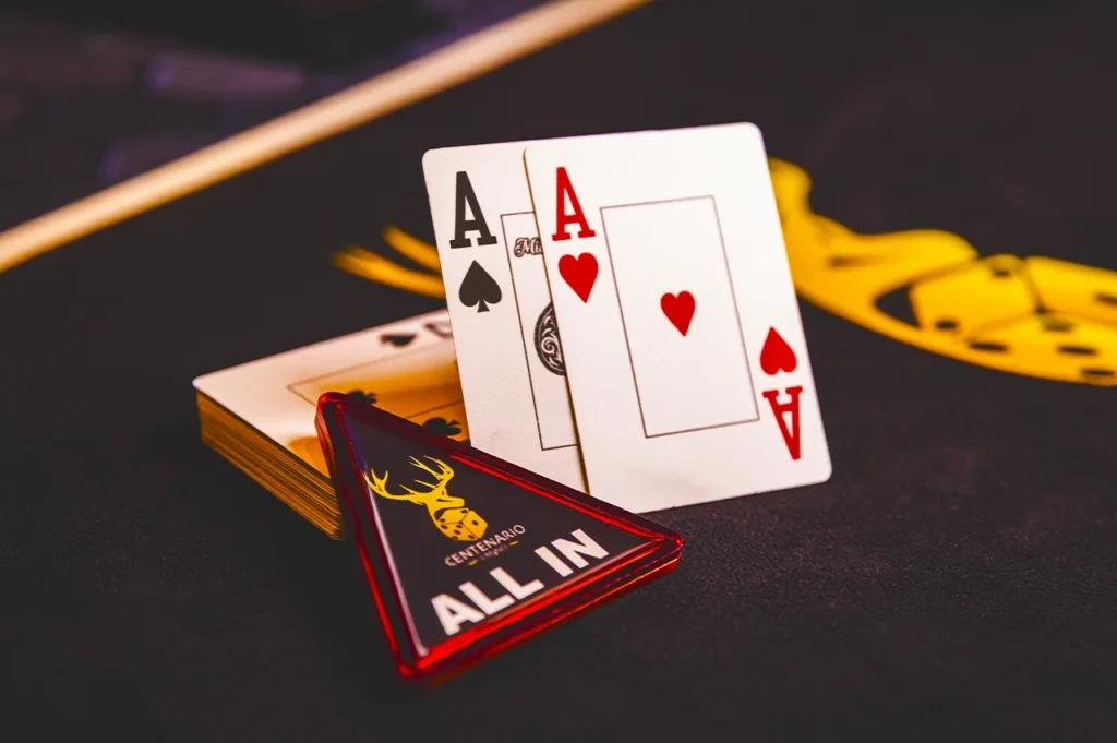 Cartas de ases y ficha de “All In” sobre mesa de póker en Casino Centenario.