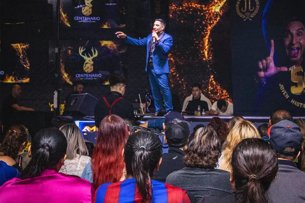 JJ El Comediante en el escenario de Casino Centenario, frente a un público que lo ovaciona.