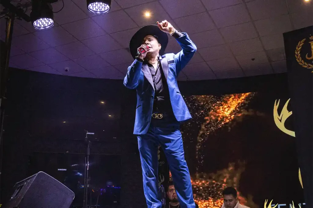 JJ El Comediante en primer plano sobre el escenario de Casino Centenario, vestido con traje azul y sombrero.